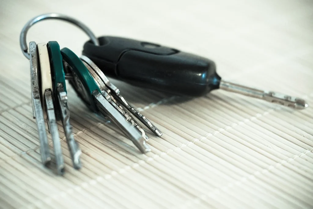 Žmogus ant darbo stalo lygina susidėvėjusį automobilio rakto korpusą su nauju pakaitiniu korpusu.