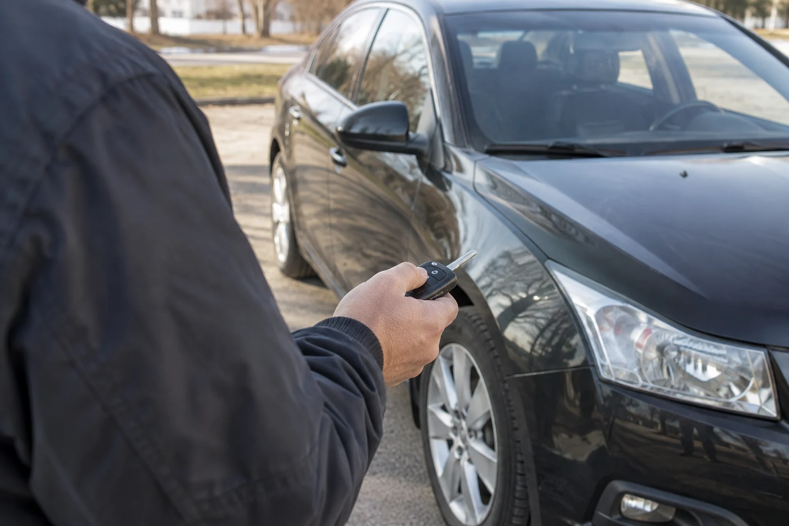 Žmogus spaudžia automobilio rakto pultelio mygtuką stovėdamas prie automobilio.